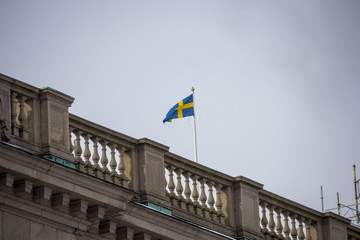 Fototapeta na wymiar Swedish flag waving in the wind. Skandinavian Sweden flag on grey sky. Stocholm