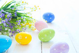 Colorful Easter eggs and spring flowers. On white wooden background