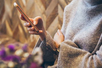 Close-up of woman's hands holding cell phone while sitting in modern coffee with wood walls. Lifestyle, reading news, social network, surfing the web / internet in smartphone. Coffee break business.