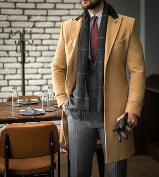 Man in custom tailored suit and trench coat posing indoors