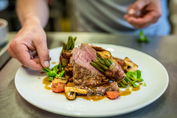 Closeup of the hands of a chef decorating a meat steak