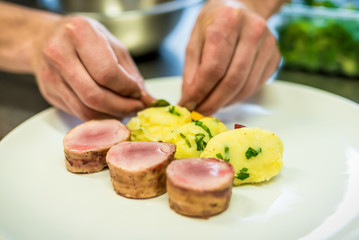 Closeup of the hands of a chef decorating a meat steak