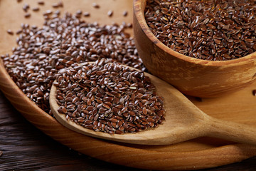 Flax seeds in bowl and flaxseed oil in glass bottle on wooden background, top view, close-up, selective focus
