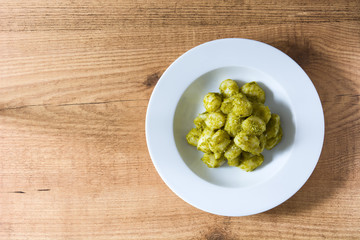 Gnocchi with pesto sauce in plate on wooden table. Top view. Copyspace