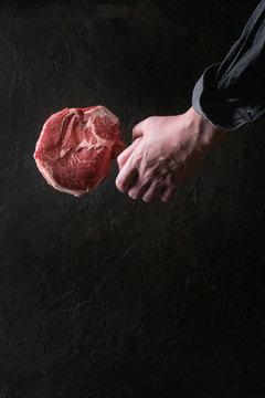 Man's hands holding raw uncooked black angus beef tomahawk steak on bone over dark background. Rustic style