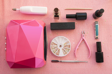 Set of equipment for manicure, pedicure and gel nail procedure on pink background. Lamp, gel...