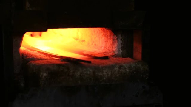 Making the sword out of metal at the forge. Heating of metal billets in the furnace. Closeup view.