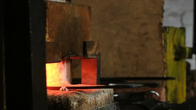 Making the sword out of metal at the forge. Heating of metal billets in the furnace. Side view.