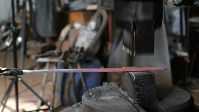 Using pneumatic hammer to shape hot metal. Making the sword out of metal. Side view.