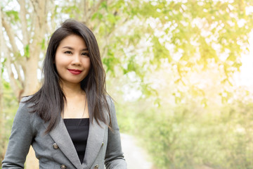 attractive young Asian business woman standing outdoors in a green park under the tree ,smiling at a camera 