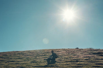 Hombre joven sentado en la loma de una montaña a contraluz al atardecer