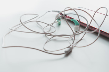 Tangled headphone wire with phone lie on white isolated background, close-up