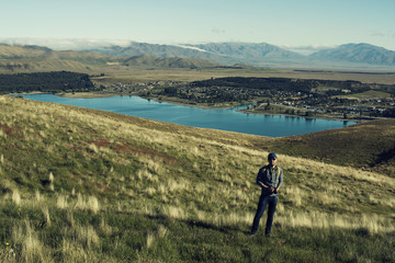 Retrato de hombre joven frente a vista de ciudad a la orilla de un gran lago en una zona montañosa con nubes aproximándose.