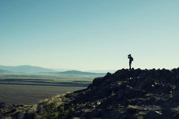 Retrato de hombre a contraluz en la cima de una montaña rocosa. Cielo azul al atardecer.
