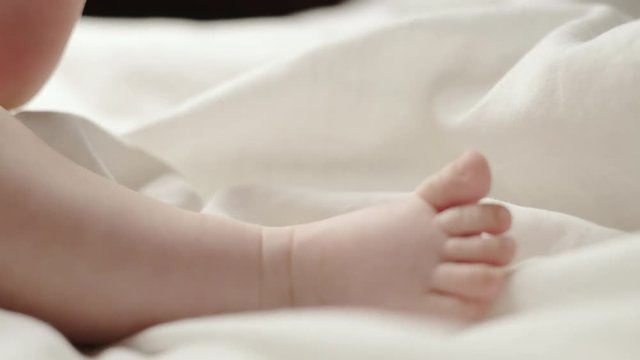 Close up on the bare feet of a newborn baby lying on its back on a white blanket kicking them in air