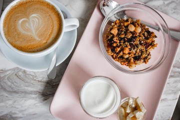 On the marble table there is a pink plate with granola