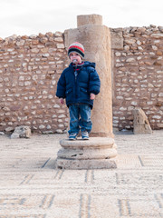 child leaning on an ancient column in ancient Roman archaeological site of Sbeitla, Tunisia