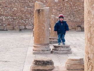 child leaning on an ancient column in ancient Roman archaeological site of Sbeitla, Tunisia