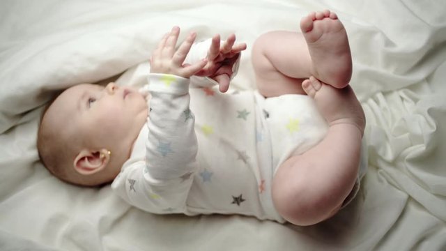 Happy contented newborn baby lying on its back on a white blanket waving its arms in the air and kicking its legs