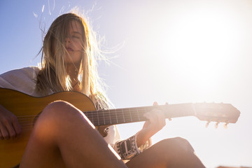 beautiful yopung woman play guitar under the sun