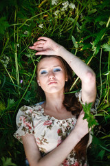 A beautiful girl in a light dress lies in a tall grass and looks into the sky. Young woman lying on the grass to relax a little. Top view, with space for text.