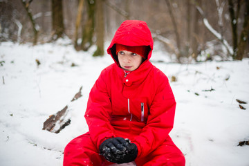 portrait of teenager dressed in red sitting in the snowy forest look engrossed