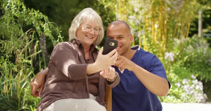 4K Happy senior lady & male nurse, posing for selfie in the garden on a sunny day. Slow motion