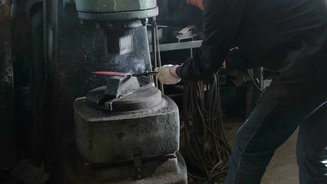 Making the knife out of metal at the forge. Man using pneumatic hammer to shape hot metal.