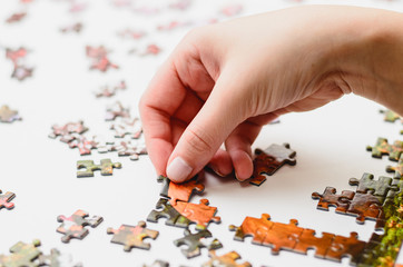 Hand of a woman playing Jigsaw Puzzle, starting to match the pieces to unveil the image. Pieces on...