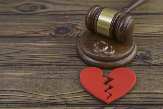 figure of a broken red heart, two wedding rings, gavel, hammer of a judge on a wooden background. Divorce proceedings, the dissolution of marriage. court, law.