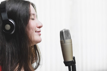 Woman singing at a studio microphone, wearing a headphone. Woman with eyes closed and a feeling...