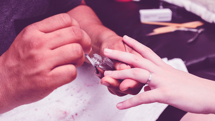 Fototapeta na wymiar Manicurist applying a transparent base on the woman hands before nail polish painting procedure.