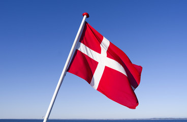 Dannebrog: The Danish national flag is fluttering in the wind at the stern of a small ferryboat crossing the Kattegat Sea