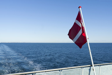 Dannebrog: The Danish national flag is fluttering in the wind at the stern of a small ferryboat...