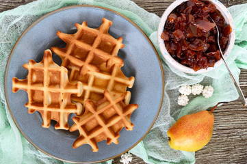 Crispy golden vanilla waffles with pear jam on a wooden background. Top view.