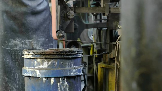 Grinding billets of metal on a belt-grinding machine. Close-up of a man's hand.