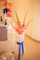 Colorful blossom gladiolus flowers in a vase decorated with blue ribbon. Wedding decoration.