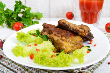 Fried pork ribs on a plate with greens and tomato juice on a white wooden background.