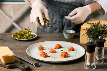Chef preparing food in the restaurant kitchen. the boss is watering salmon carpaccio with olive oil