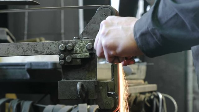 Grinding billets of metal on a belt-grinding machine. Close-up of a man's hand.