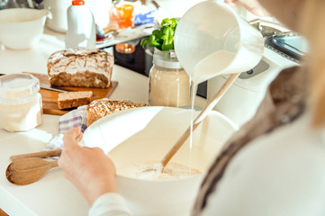 Woman in the kitchen pours measured milk into a bowl with flour