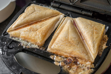 A toasted sandwich cooking in a toasted sandwich maker.