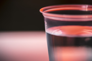 Transparent plastic glass with transparent liquid in it on a red and grey disco scene