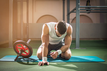 Tired muscular man taking break after training with ab wheel at gym.