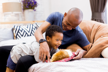 African American family of two playing with a dog pet in bedroom