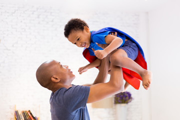 Father lifting son up with super hero costume at home