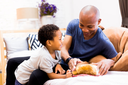 African American Family Of Two Playing With A Dog Pet In Bedroom