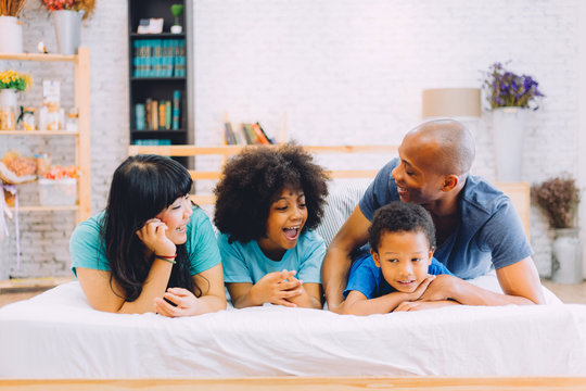 Happy African American Family Laying On Bed At Home, Happily Talking To Each Other. Parenthood And Family Concept