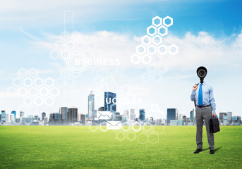 Camera headed man standing on green grass against modern cityscape