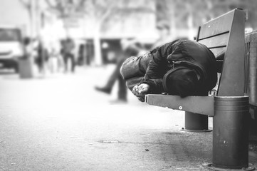Poor homeless man or refugee sleeping on the wooden bench on the urban street in the city, social...
